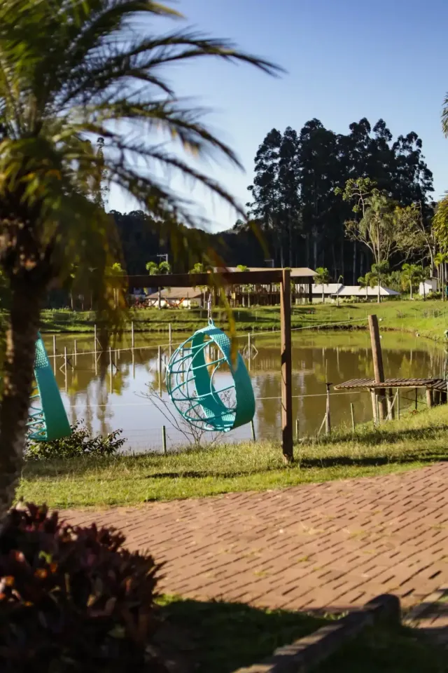 Lagoa do parque com cerca de madeira, palmeiras e um campo gramado sob um céu azul claro.