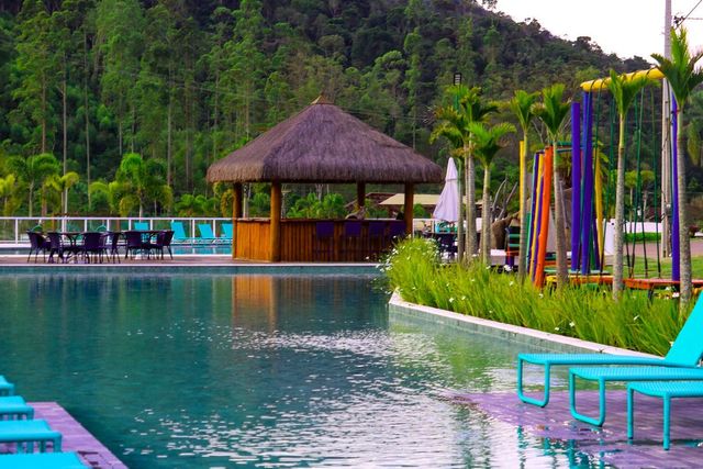 Piscina do resort com água turquesa, espreguiçadeiras, cabana de palha e vegetação tropical ao lado de uma encosta.