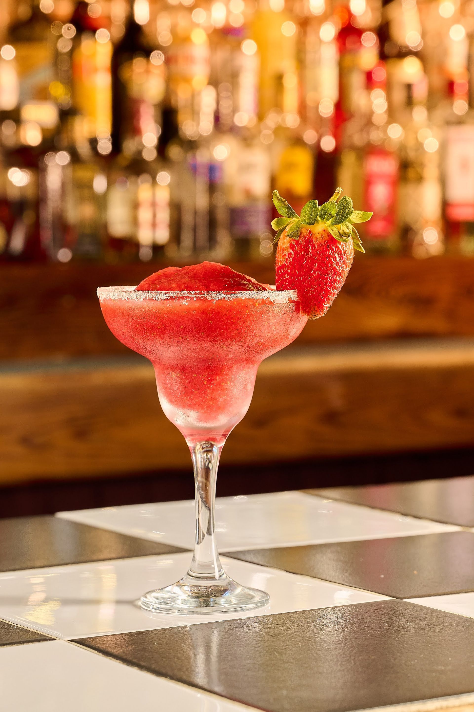 Una margarita de fresa en una copa de martini sobre una mesa a cuadros.