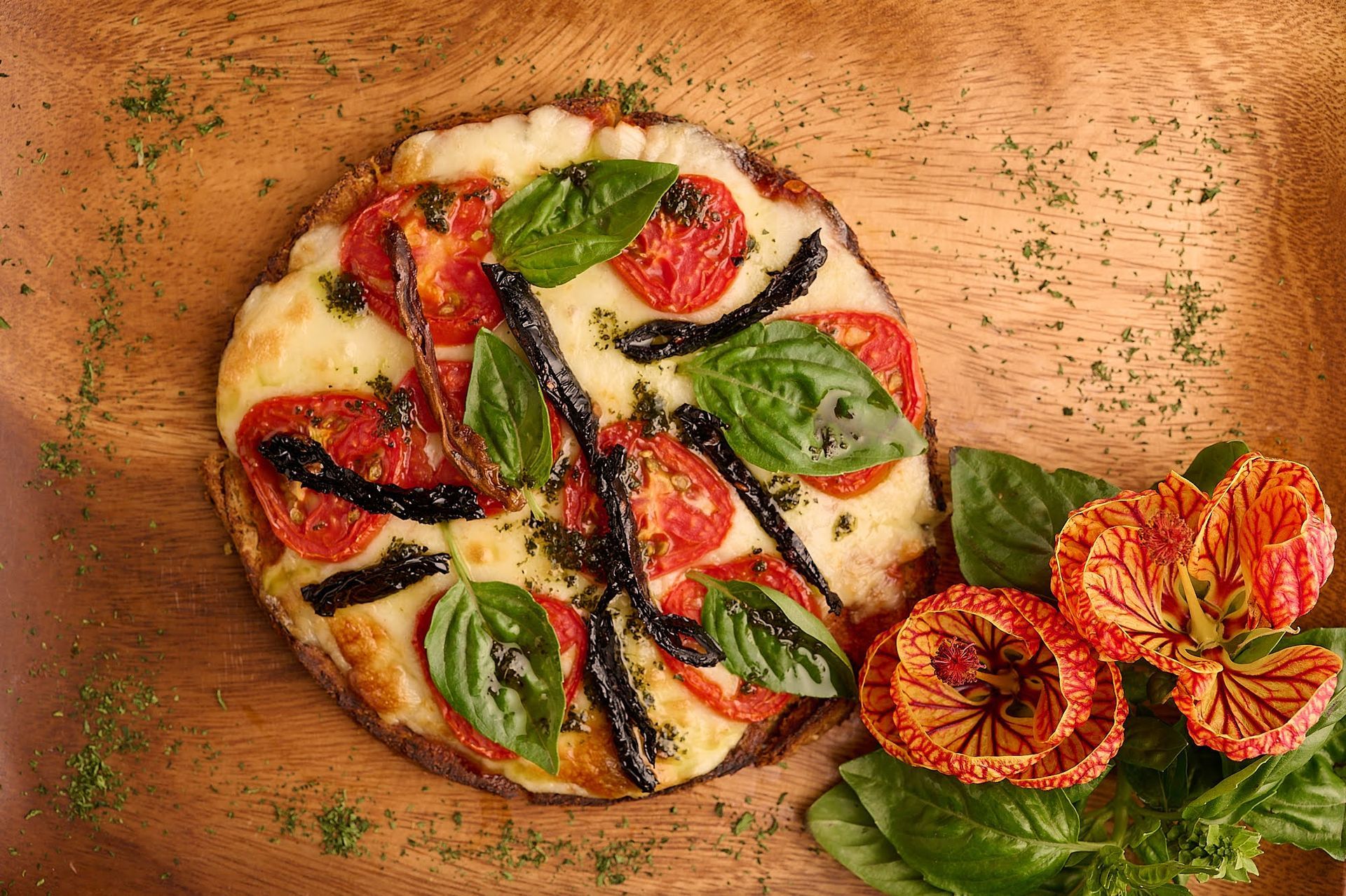 Una pizza con tomates y albahaca sobre un plato de madera.