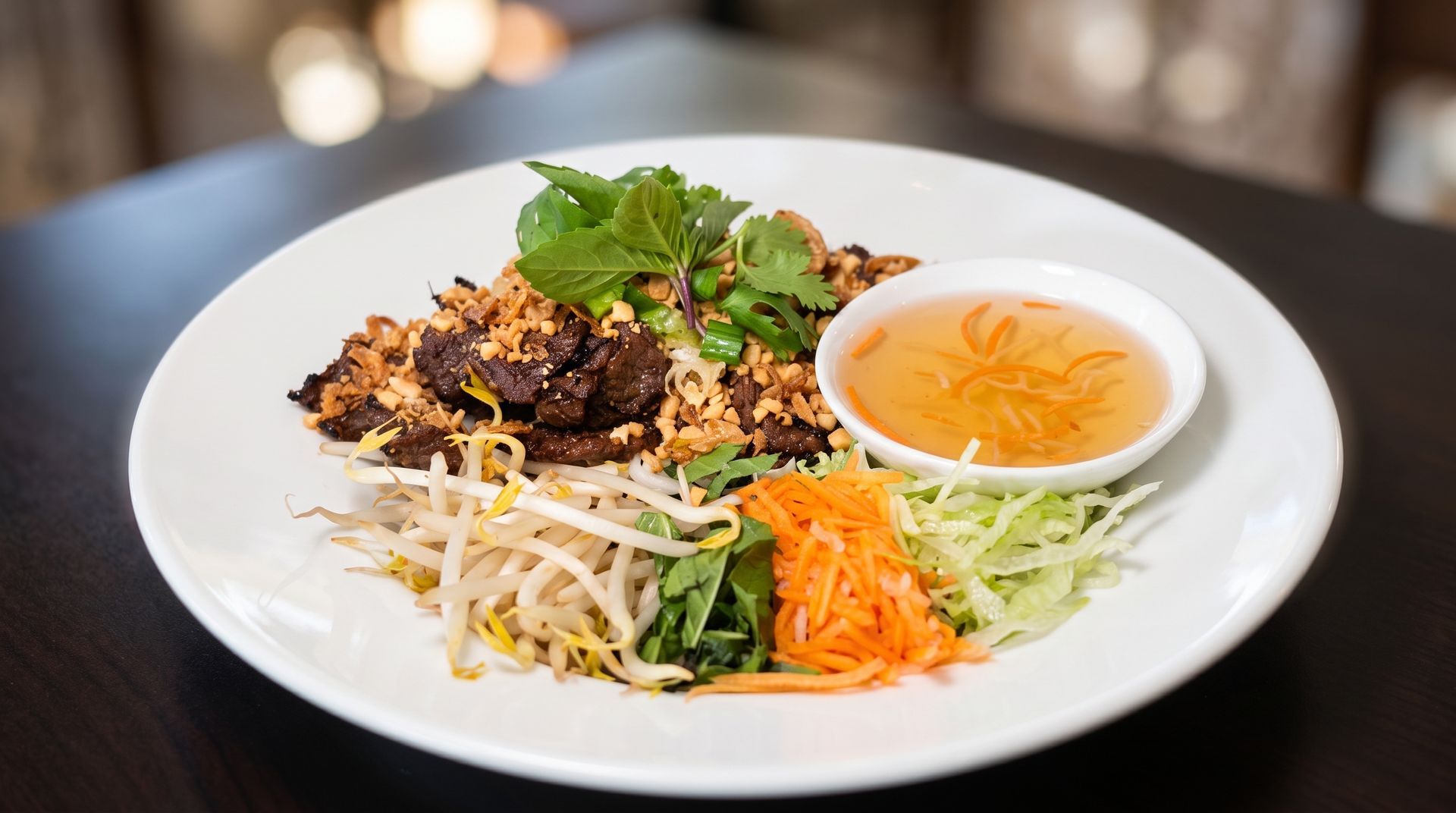 White plate of Vietnamese vermicelli with grilled meat, herbs, bean sprouts, and dipping sauce