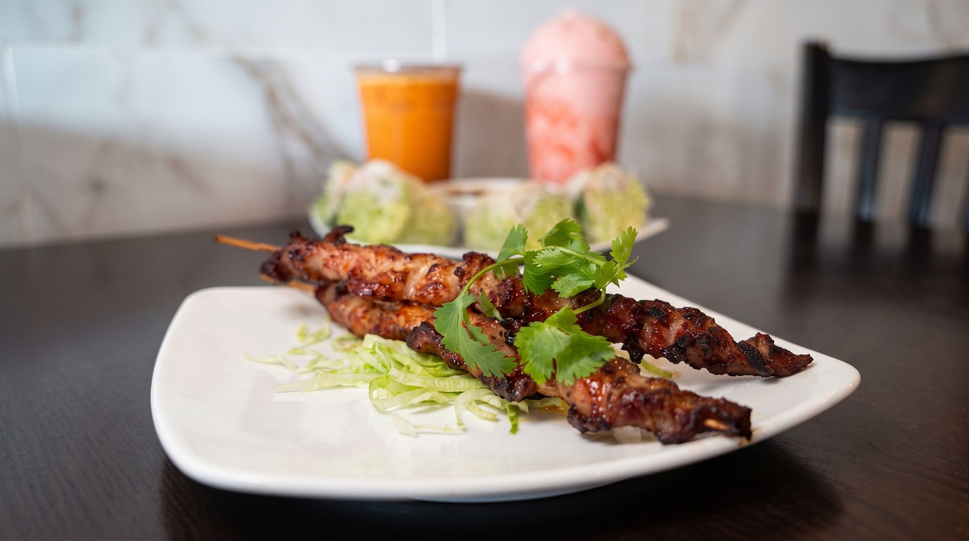 Grilled meat skewers on a white plate with lettuce garnish on a dining table