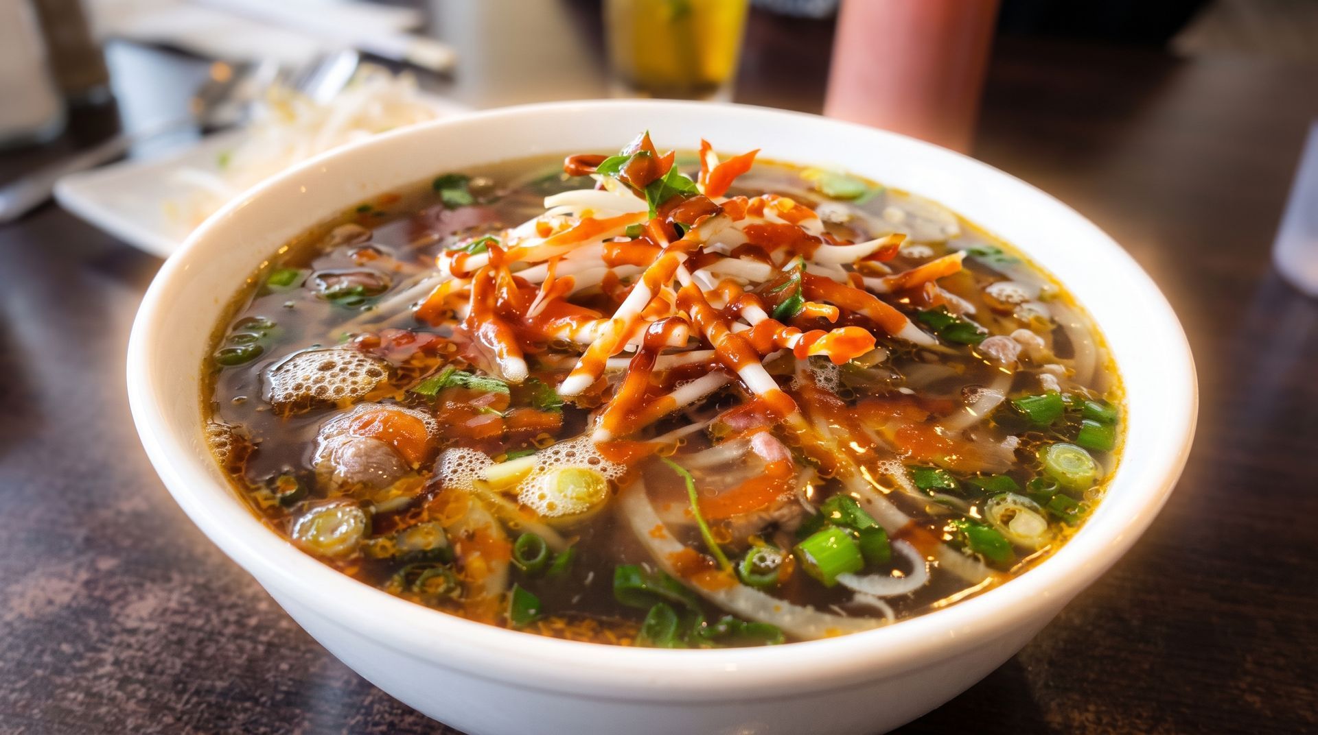Bowl of steaming soup topped with shredded vegetables and herbs on a table