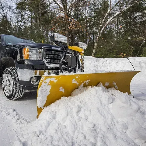 A yellow snowplow clearing snow from a driveway, attached to a black truck.