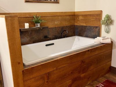 White bathtub encased in rustic wood paneling, with a small shelf holding a candle and plant.