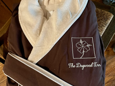 Brown bathrobe with cream-colored trim, featuring a floral logo and 
