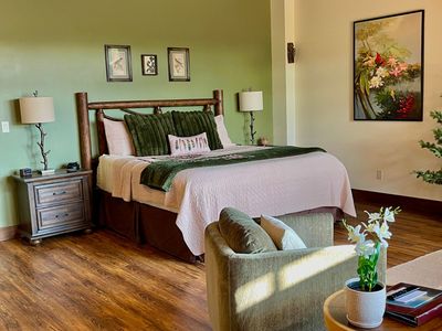 A cozy bedroom with wood paneling, a large bed, armchairs, and a blue rug.