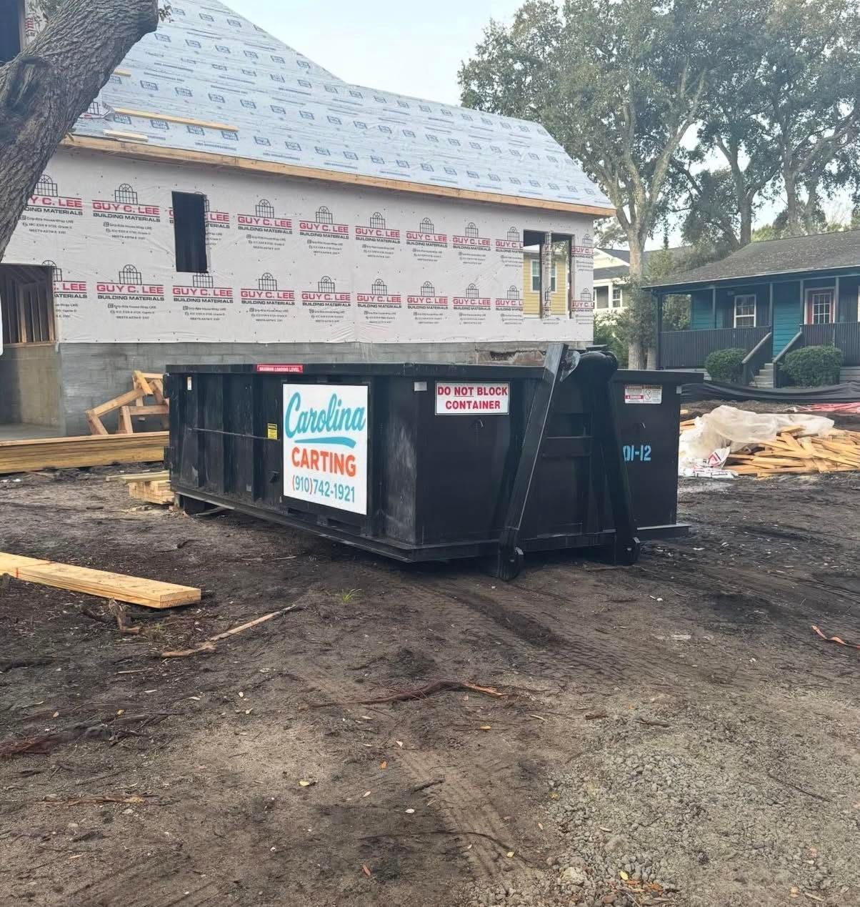 Two black dumpsters outside a house under construction on a dirt lot