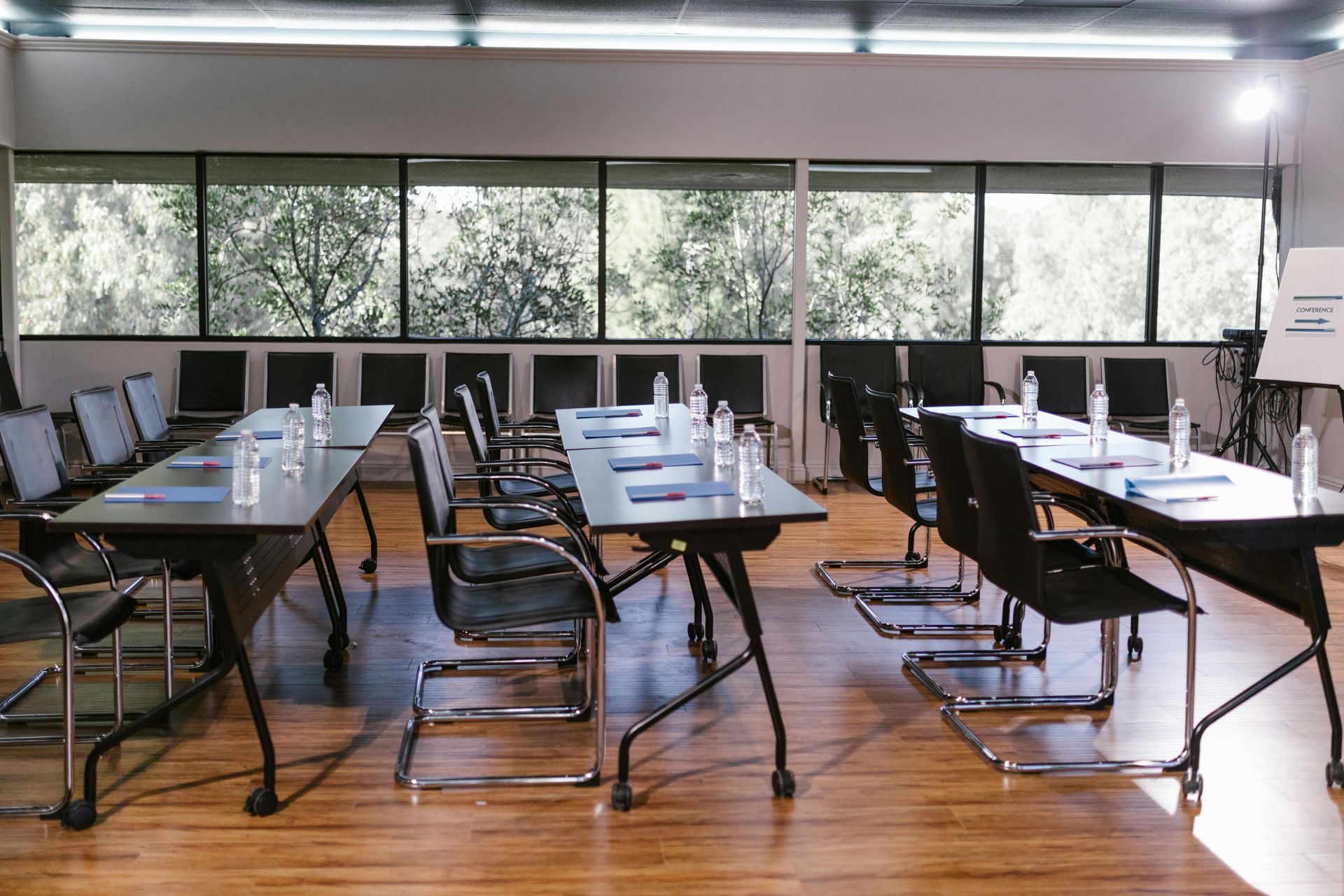 Conference room with long tables, chairs, and a window with a view of trees.