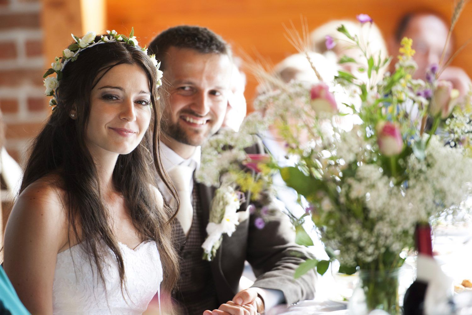 Bride and groom smiling at a wedding reception with floral arrangement in the foreground.
