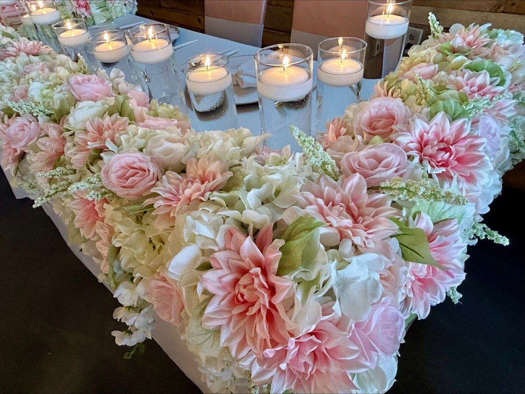 Floral arrangement with candles on a mirrored surface, featuring light pink and white blooms.