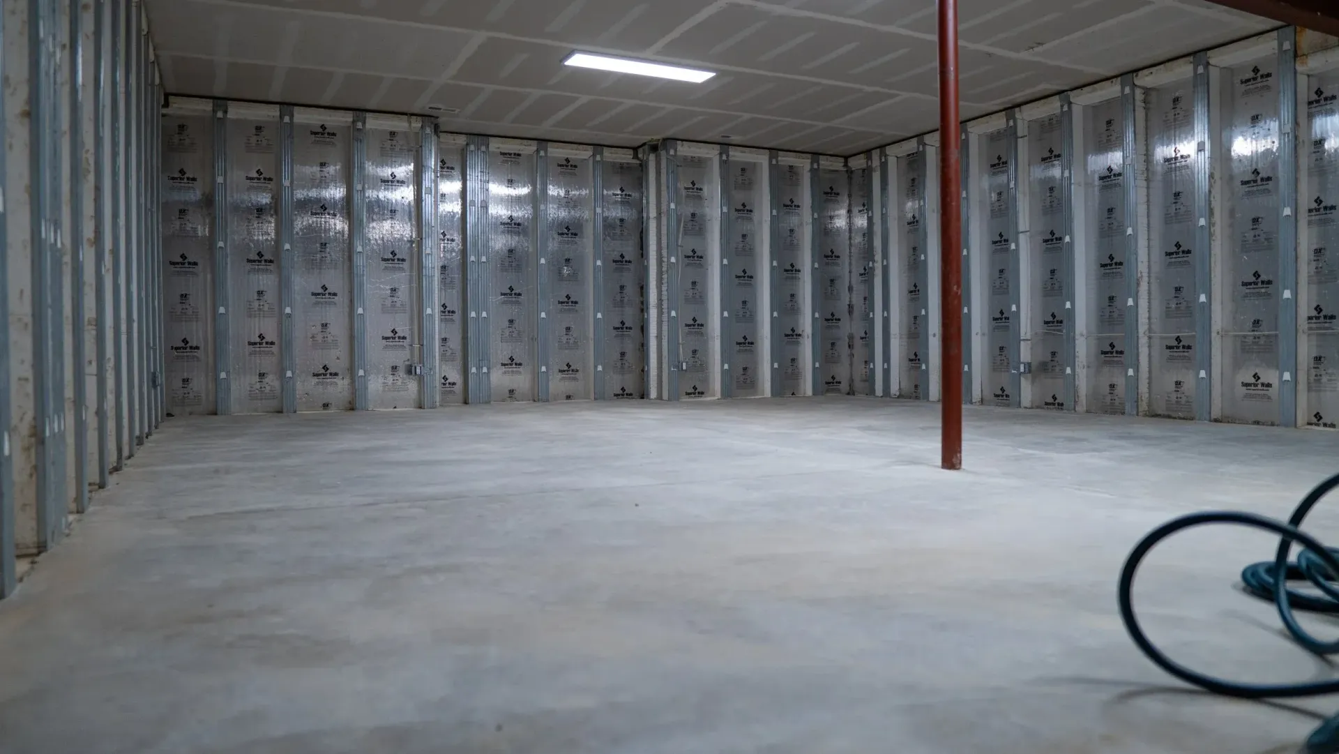 An unfinished basement room with a concrete floor, metal stud framing on the walls, and insulation backing.