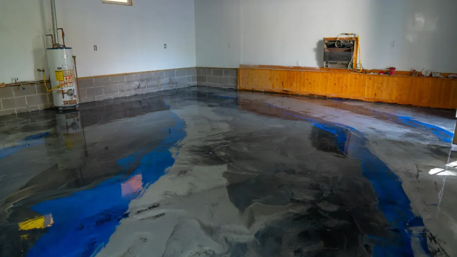 A basement with a glossy, blue and grey epoxy floor, a water heater, and wood-paneled walls.