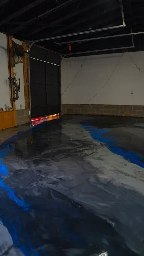 A garage interior with a glossy, poured epoxy floor featuring swirled patterns of gray, black, and vibrant blue.