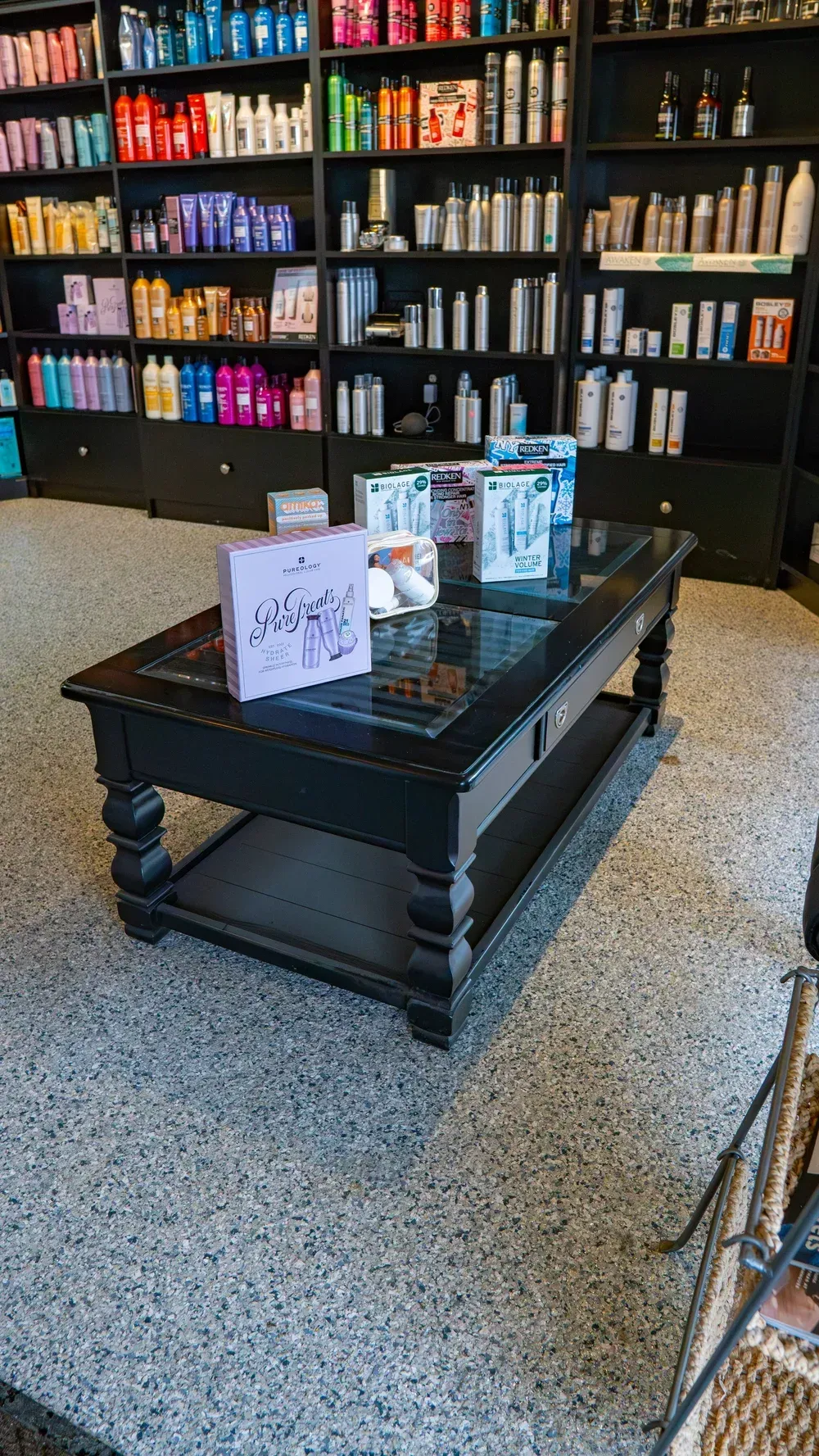 A black coffee table holding retail products sits in front of shelves stocked with hair and beauty supplies.