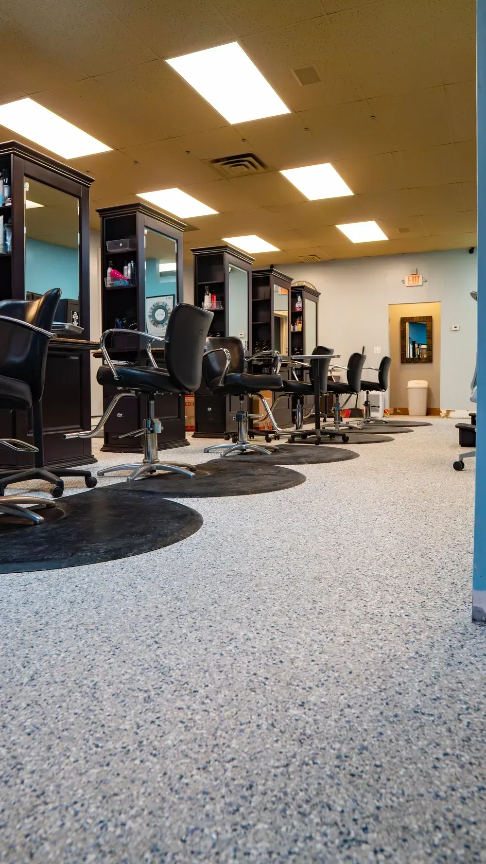 A hair salon interior with a row of styling chairs facing mirrors and a speckled floor.