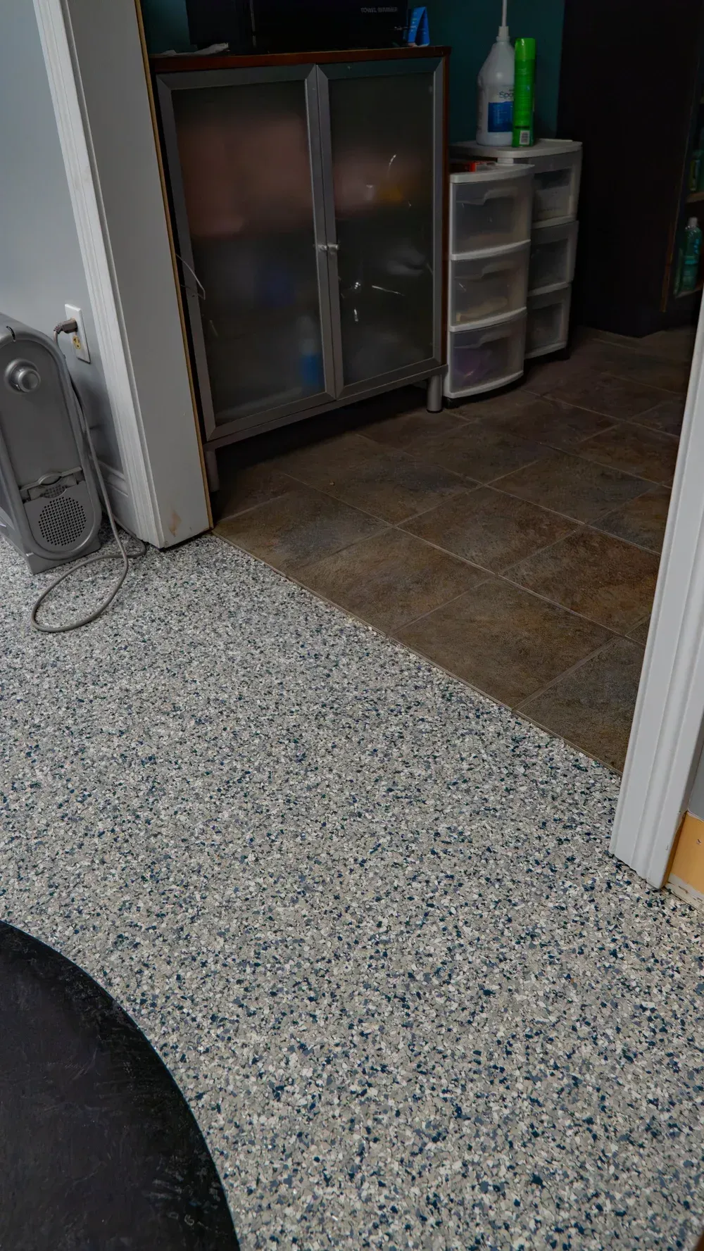 A transition between a white, blue, and gray speckled floor and a brown tiled floor, with a metal cabinet and drawers.