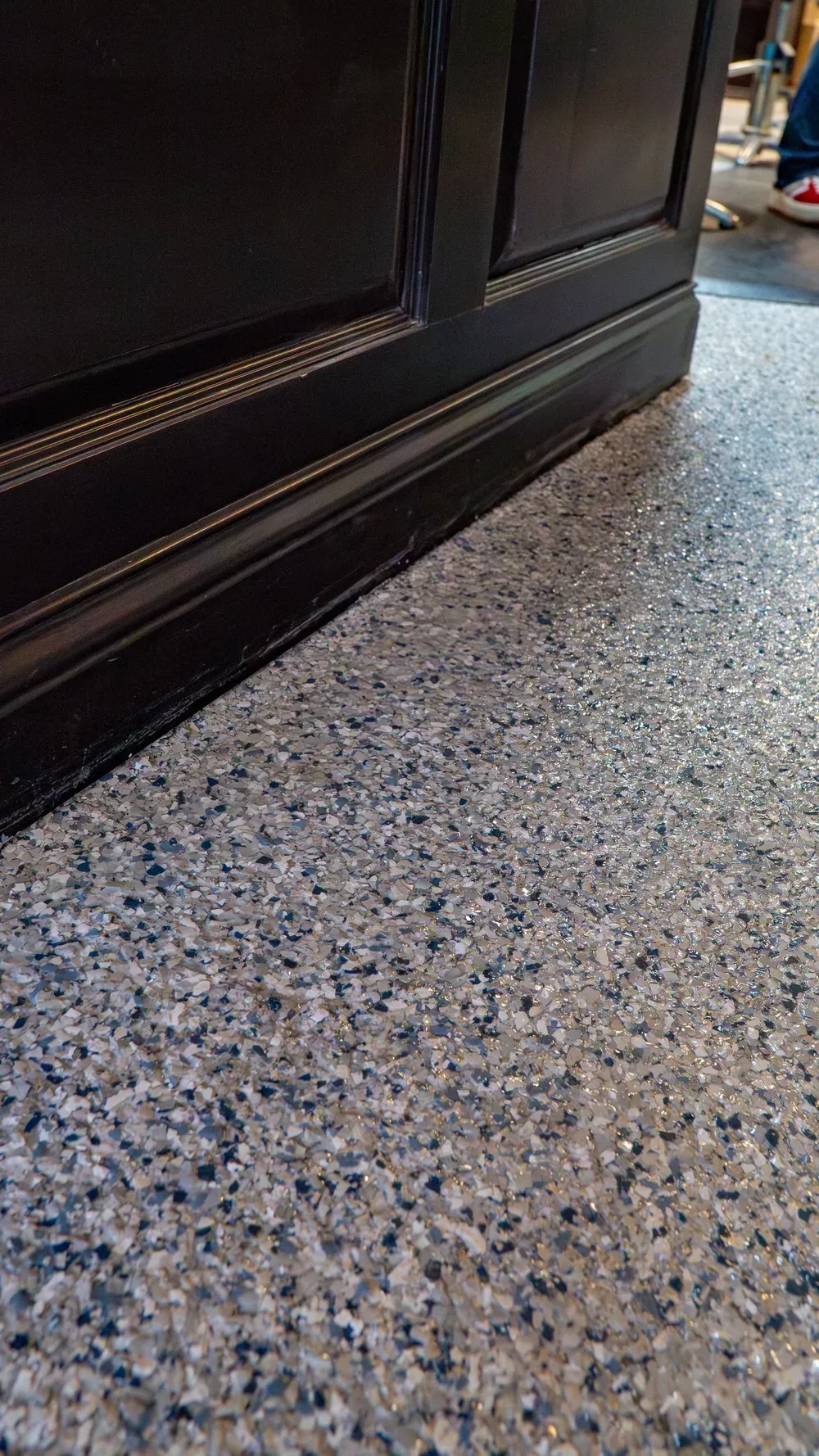 A close-up view of the base of a dark wood cabinet resting on a gray, speckled terrazzo floor.