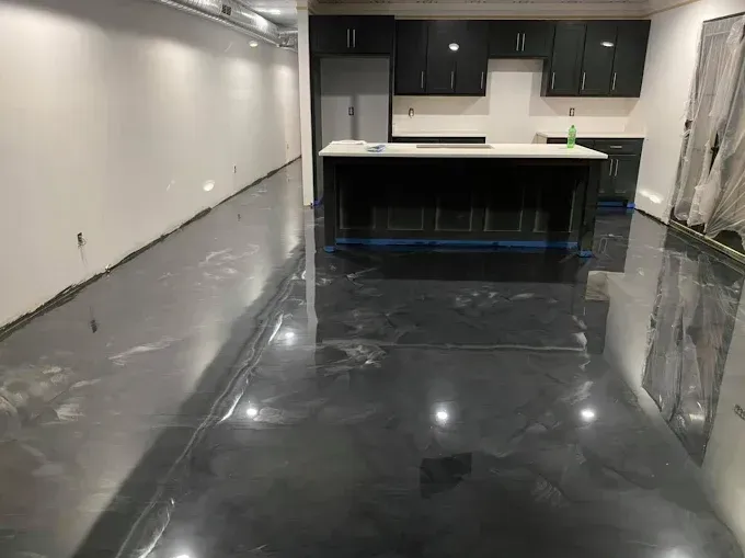 A modern kitchen with dark cabinetry, a white-topped island, and a reflective, metallic gray epoxy floor.