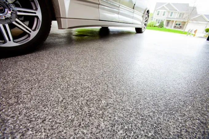 A silver car parked on a speckled, grey epoxy garage floor with a suburban home visible in the background.