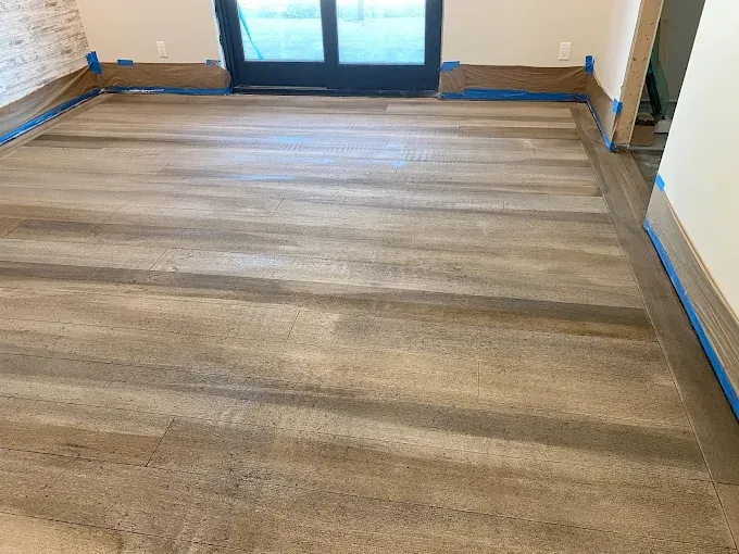 Newly installed wood-look laminate flooring in a room with blue painter's tape along the baseboards.