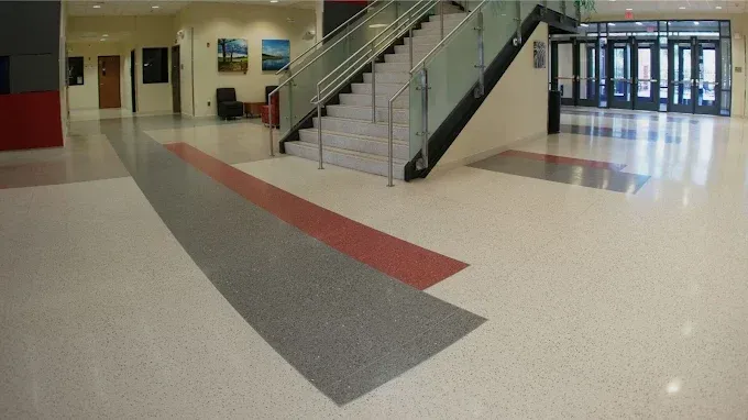 A wide-angle view of a building interior featuring a modern staircase, light flooring, and grey and red accent rugs.