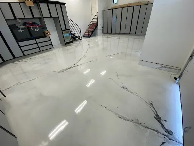 A garage with white epoxy flooring featuring black marbled veins, metal storage cabinets, and an industrial staircase.