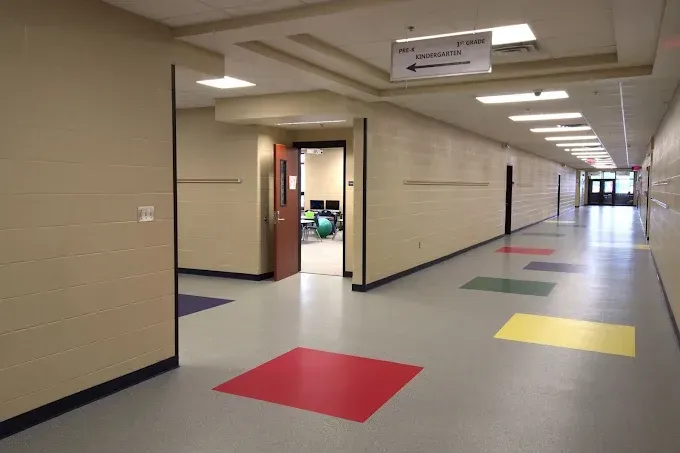 Long school hallway with beige walls, an open door to a classroom, and colorful floor squares leading down the corridor.