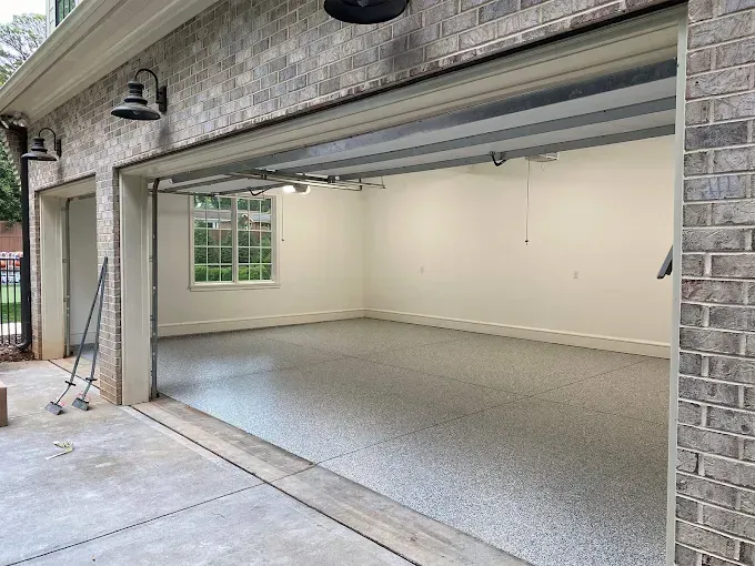 A spacious garage with an open door, light-colored walls, and a speckled gray epoxy floor.