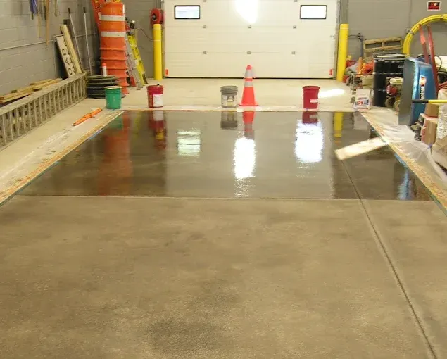 A large indoor concrete floor shows a clear contrast between a polished, reflective section and raw, matte concrete.