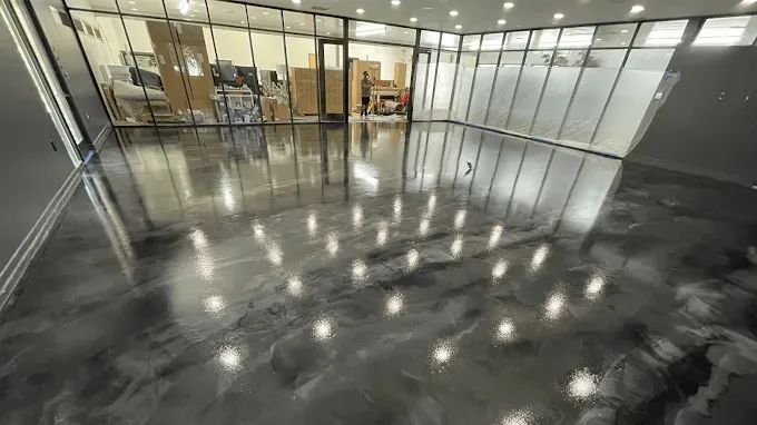 A wide, empty room featuring a high-gloss, metallic grey epoxy floor with reflections of overhead recessed lighting.