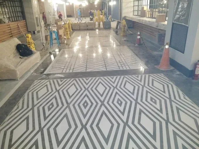A room under construction with a geometric diamond-patterned floor, safety cones, and building materials in the background.