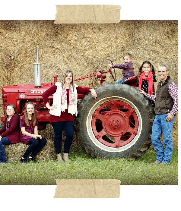 Group posing by a red tractor in a hayfield, with several people leaning and standing around the large wheel