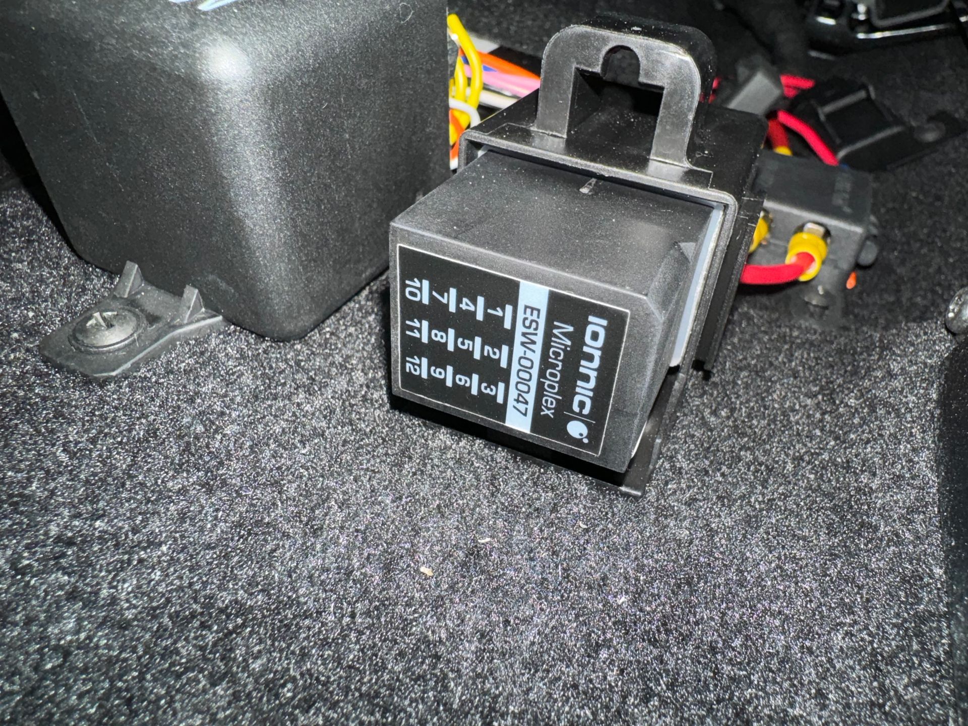 Black relay module with labels, sitting on gray carpet near a black box.