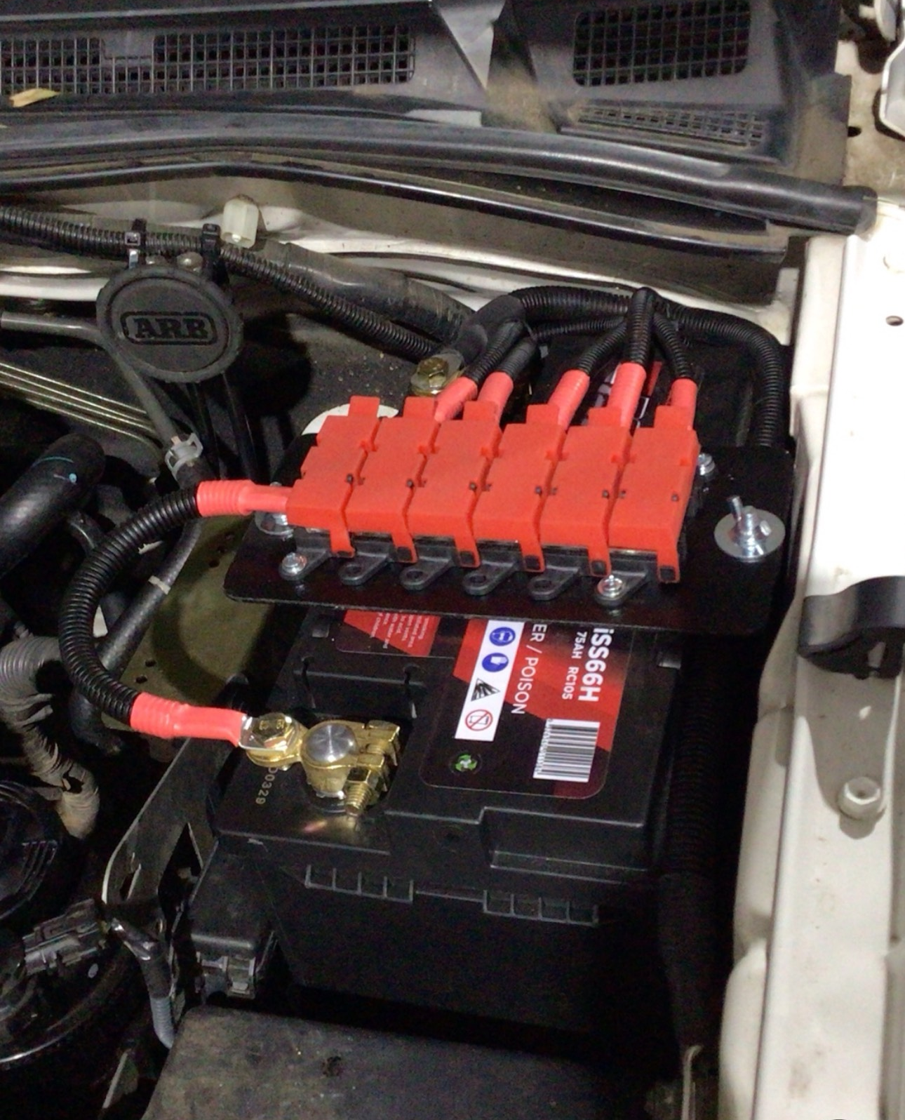Battery with red fuse holders, mounted in an engine compartment.