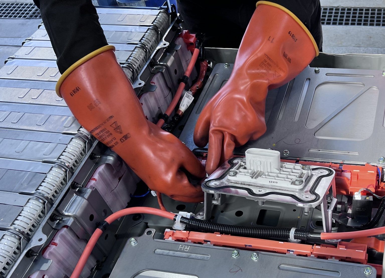 Hands wearing orange gloves assembling electrical components in a battery pack.