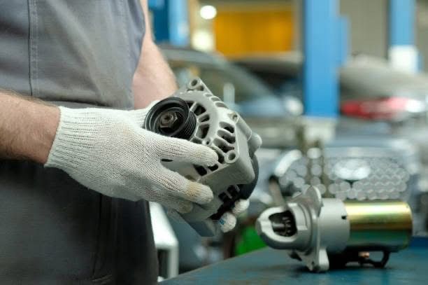 Mechanic holding a car alternator, working in an auto repair shop.