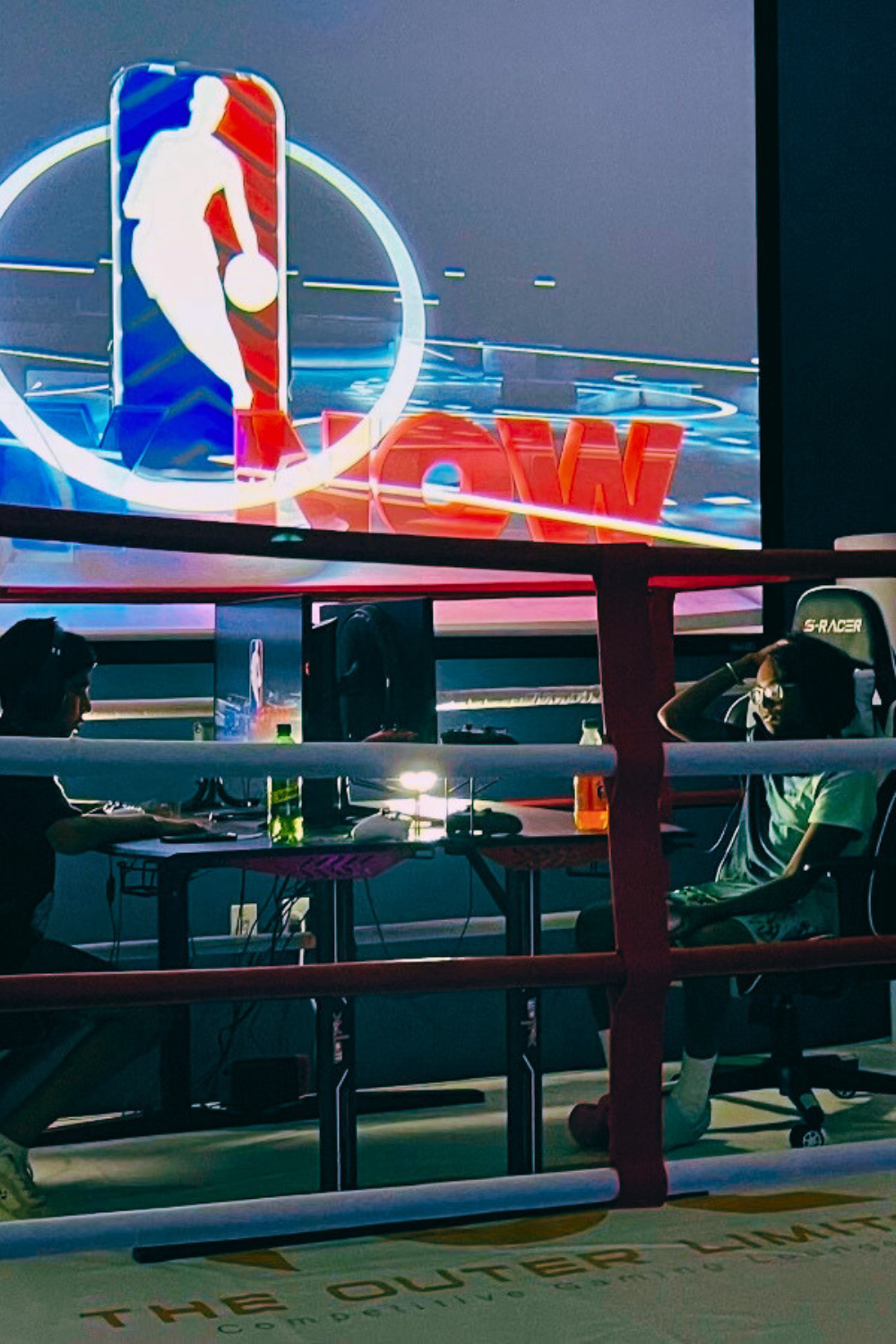 A group of people are sitting in front of a large screen with the nba logo on it.