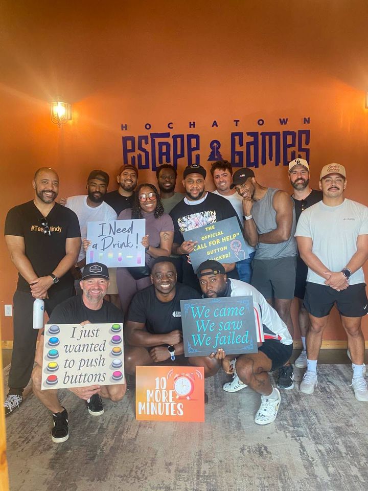 Group posing inside a venue with orange walls, holding colorful signs under a “PSOR & GAMES” banner.