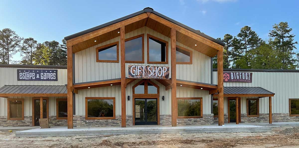 Front view of a rustic two-story building with wood beams, stone accents, and large windows under a cloudy sky