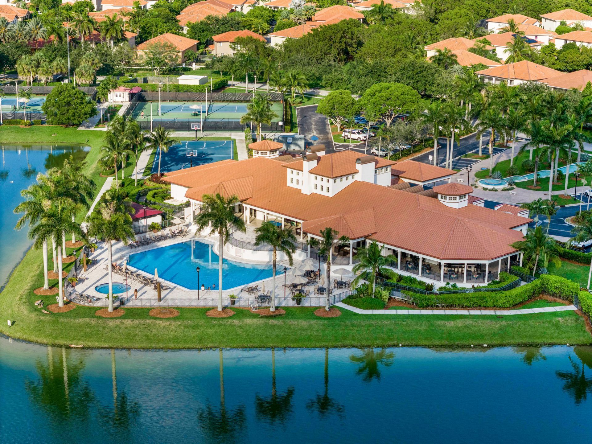 Aerial view of a tropical resort with a pool, red-roofed buildings, palm trees, and a lagoon.