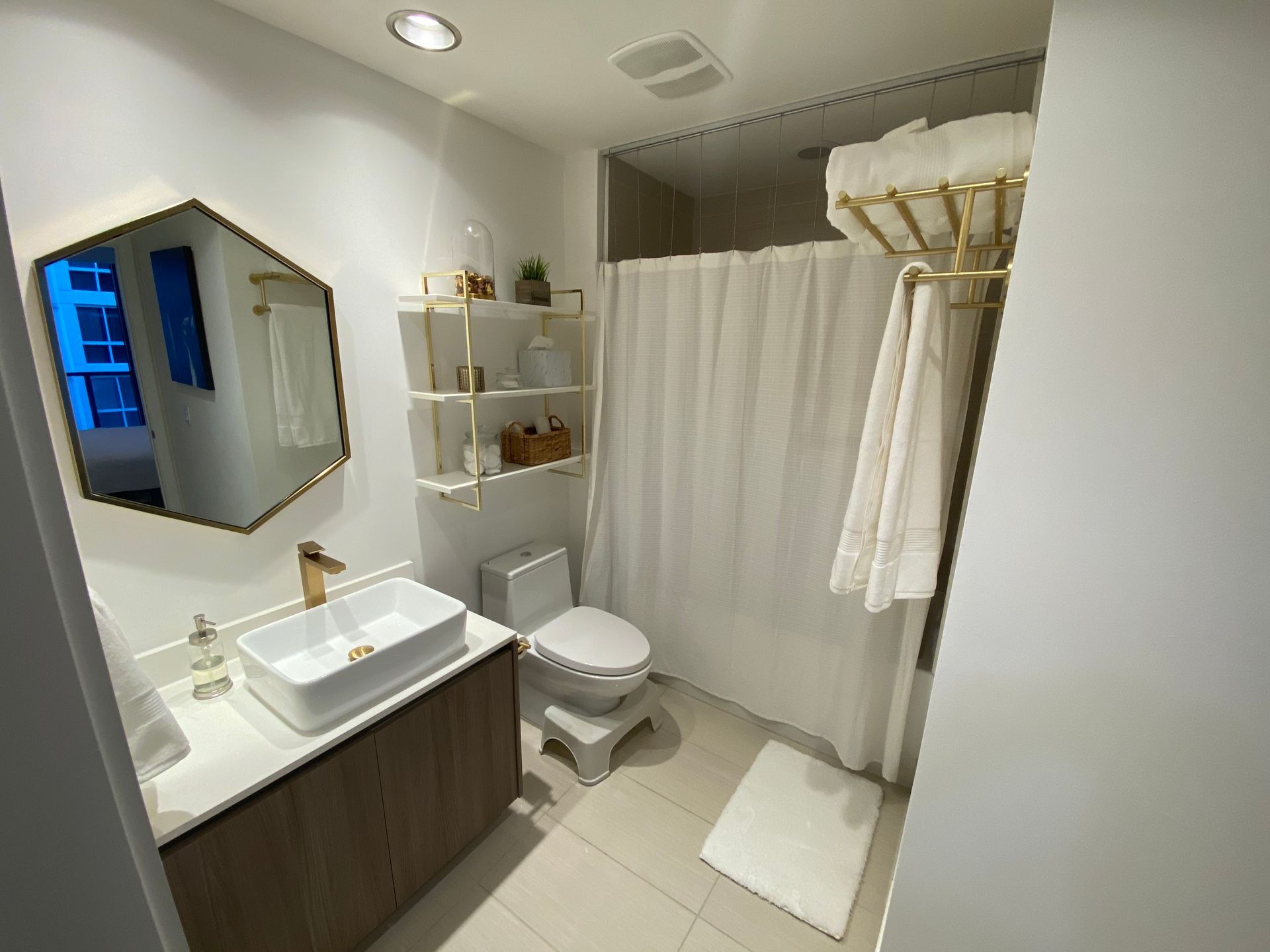 Modern white bathroom with vanity, sink, toilet, shower curtain, towel rack, and bath mat