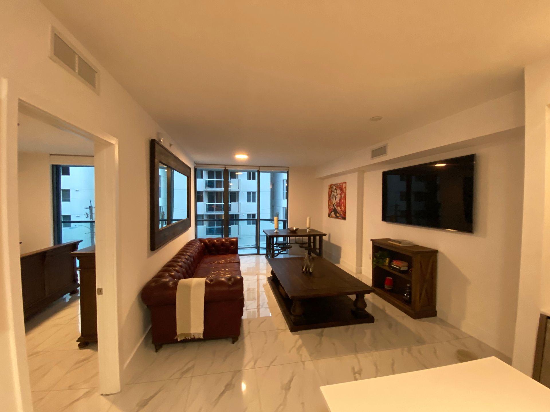 Modern living room with sofa, coffee table, wall-mounted TV, and balcony view through large windows
