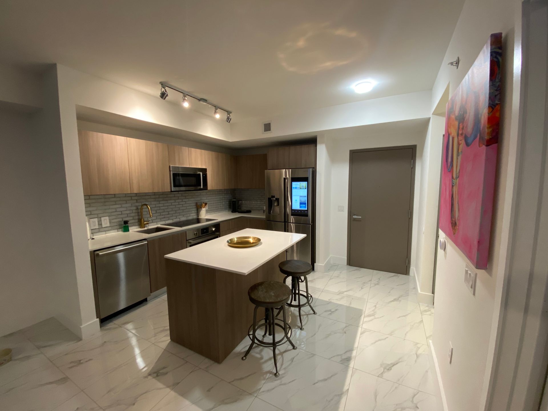 Modern kitchen with island, stainless appliances, and track lighting in a bright open apartment