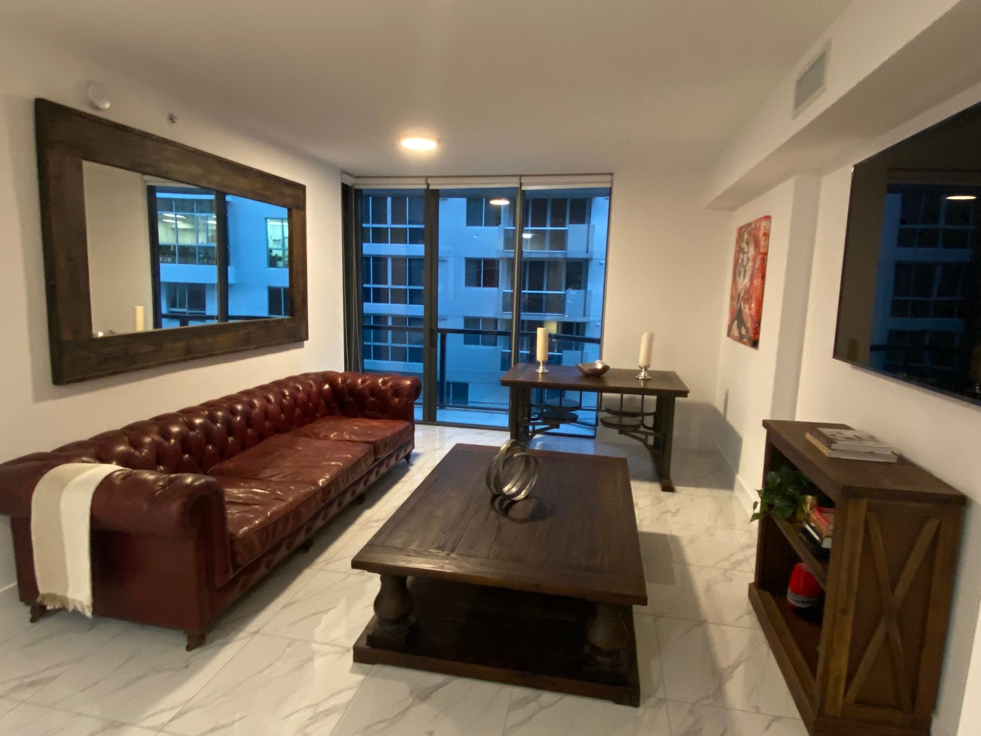 Modern living room with red sofa, dark coffee table, side table, and city view through large windows