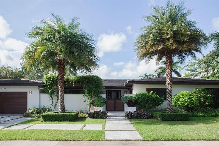 Single-story suburban house with two palm trees, a garage, and a front walkway under a blue sky