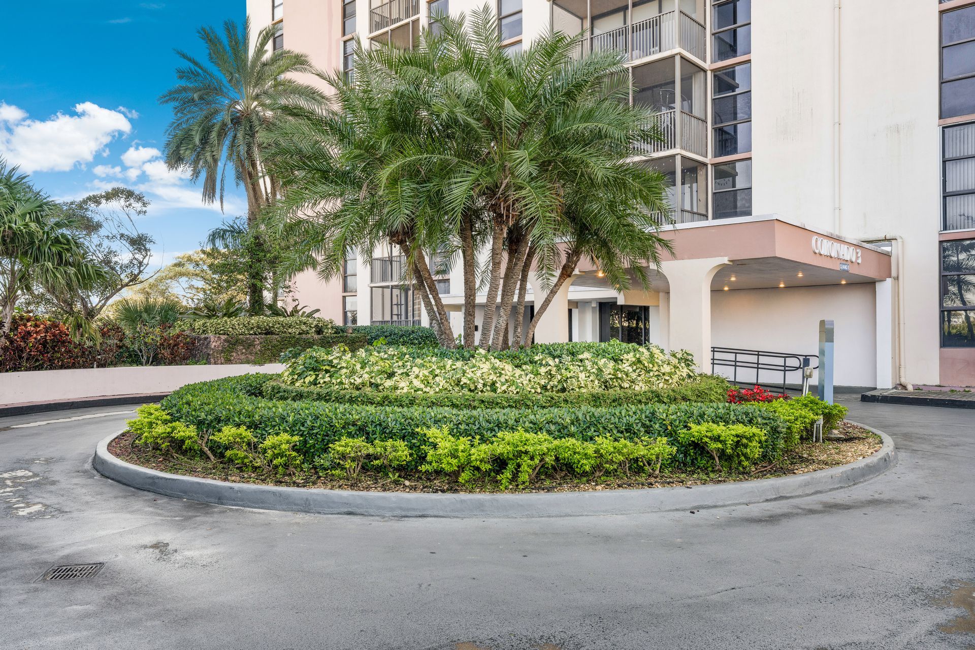 Roundabout with green shrubs and palm trees beside a modern apartment building