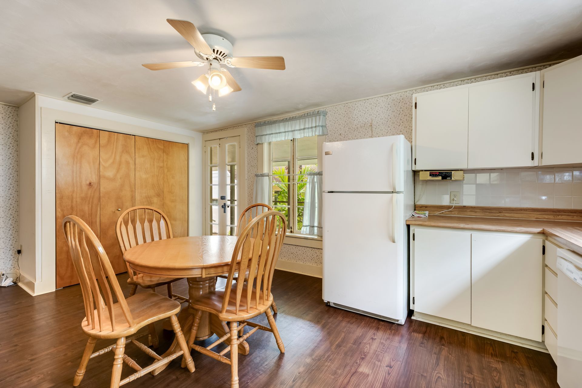 Small kitchen with round wooden table, chairs, white appliances, cabinets, and wood floor