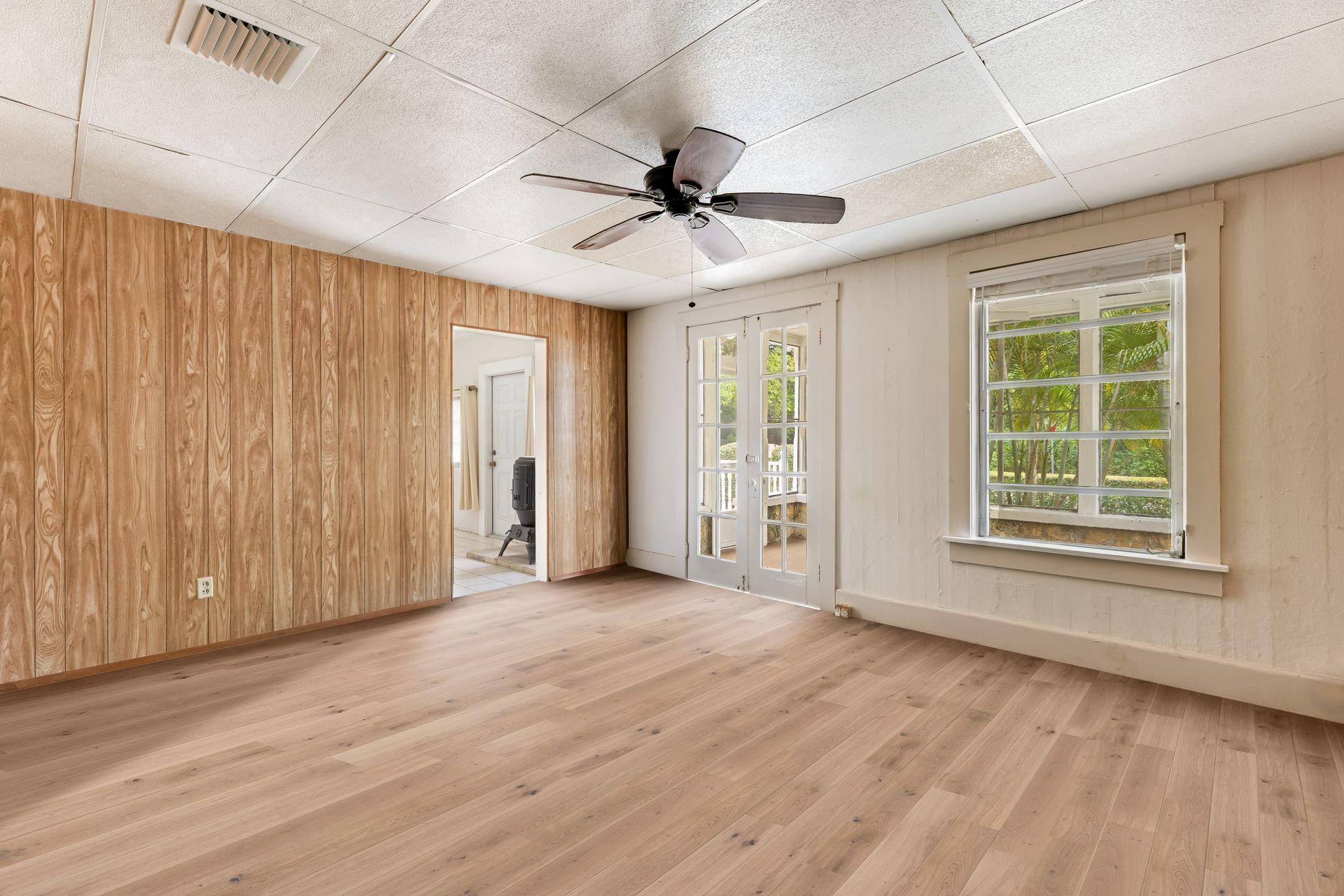 Empty room with wood-paneled wall, light flooring, ceiling fan, and windows with white trim