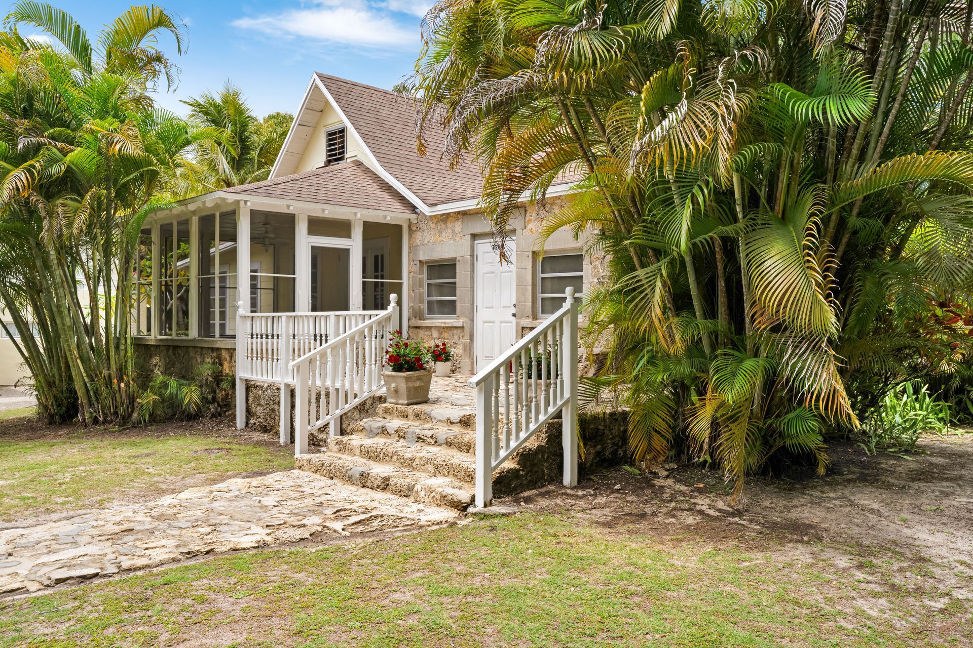Small white cottage with a front porch, steps, and tropical palm trees surrounding it